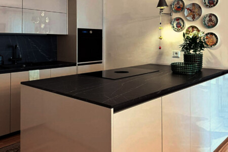 Beige high-gloss kitchen with black marble countertop, decorative painted wall plates and green planter detail